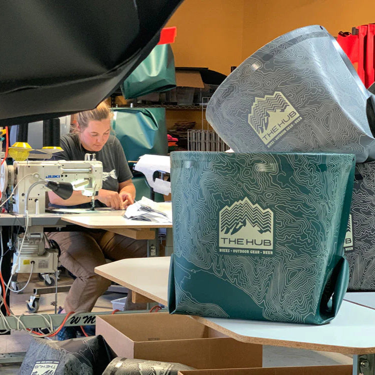 Person working at a sewing machine with 'The Hub' branded bags in the foreground.
